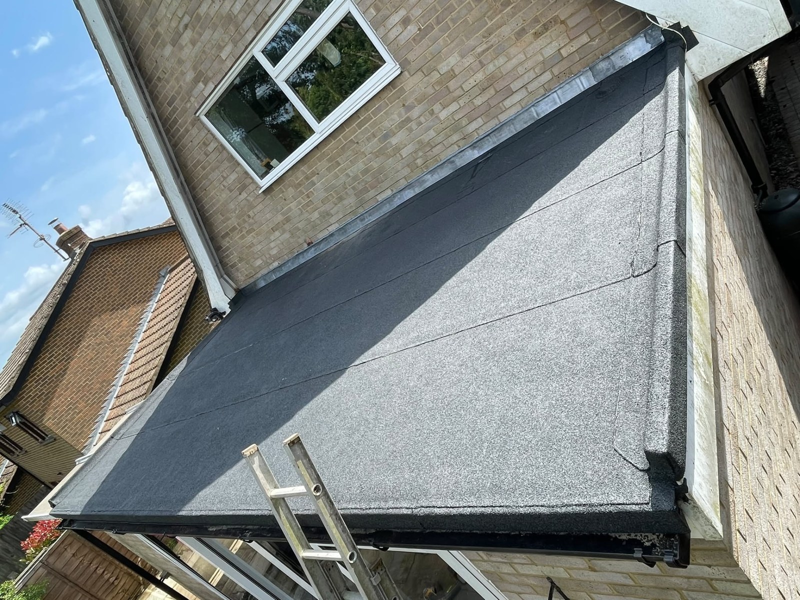 Completed torch-on felt flat roof with lead flashing to the abutting brick wall